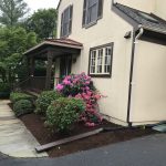 Landscaped garden bed with pink flowering shrubs beside a residential home