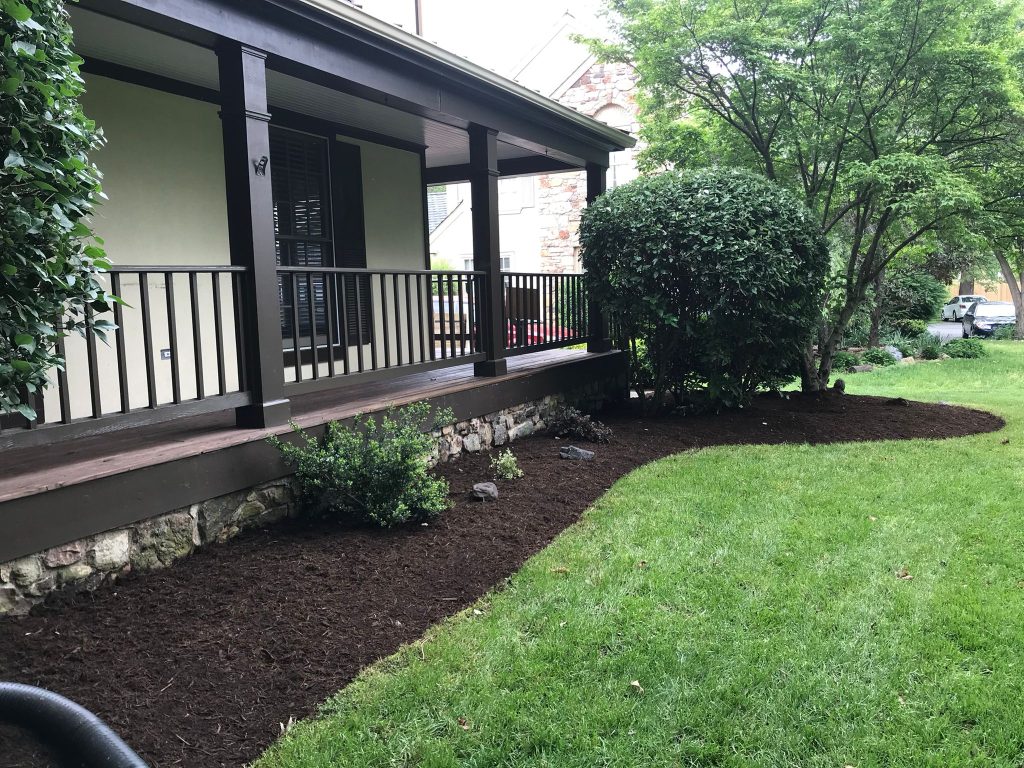 Mulched foundation garden bed with shrubs and flowers beside a front porch